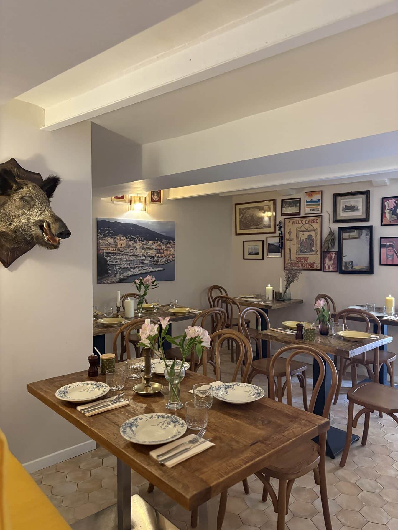 La salle du bistrot : table dressée, chaises en bois courbé et murs couverts de cadres anciens.