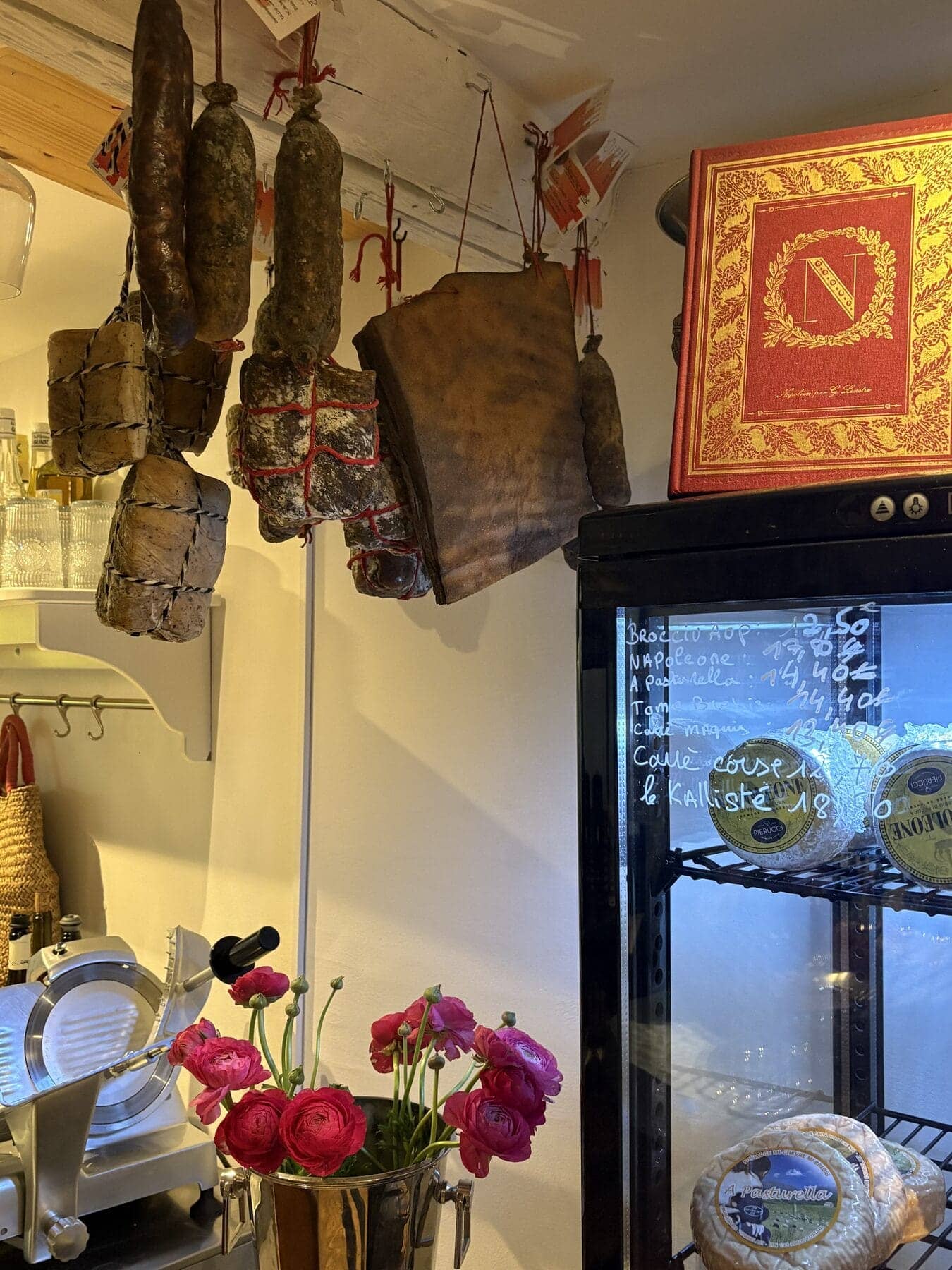 Vitrine réfrigérée et charcuteries suspendues de l’épicerie fine corse : le lieu où l’on choisit ses fromages de brebis frais.
