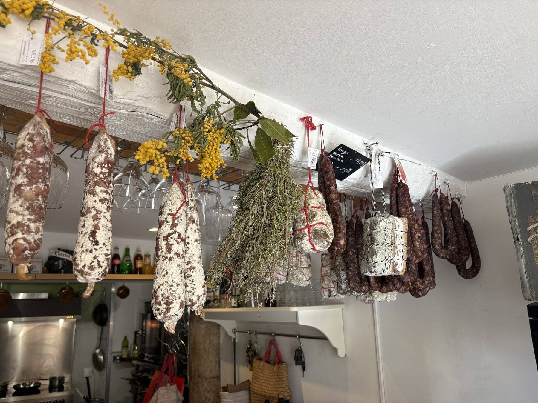 Charcuteries corses — saucissons, coppa et lonzu — suspendues au plafond de l’épicerie fine du Bistrot Napoléon à Hyères.