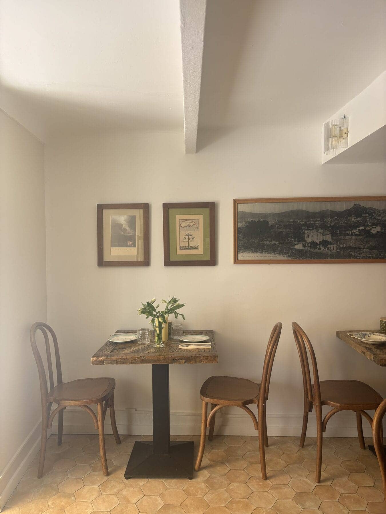 Coin de salle intimiste du Bistrot Napoléon à Hyères : tables en bois brut, chaises bistrot et mur d’objets chinés, prêt à réunir une famille pour un baptême.