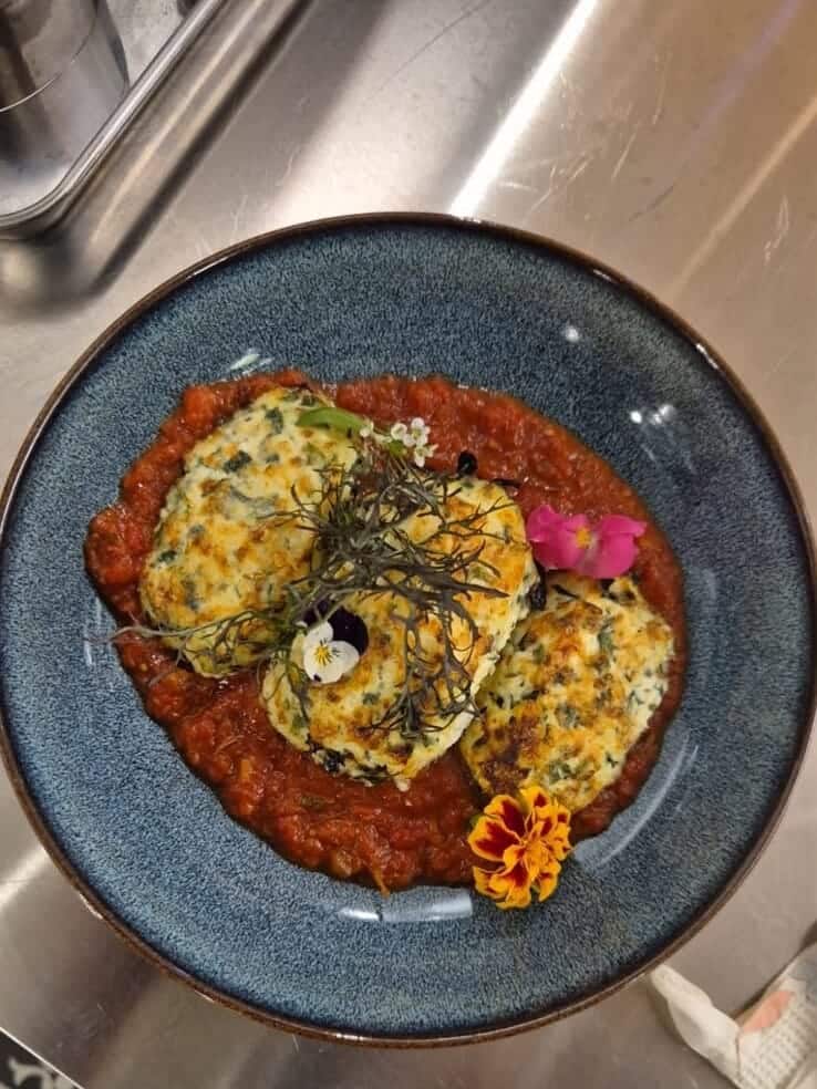 Storzapretti : quenelles de brocciu gratinées à la tomme de brebis, sur une sauce tomate aux herbes du maquis, dans un bol bleu.