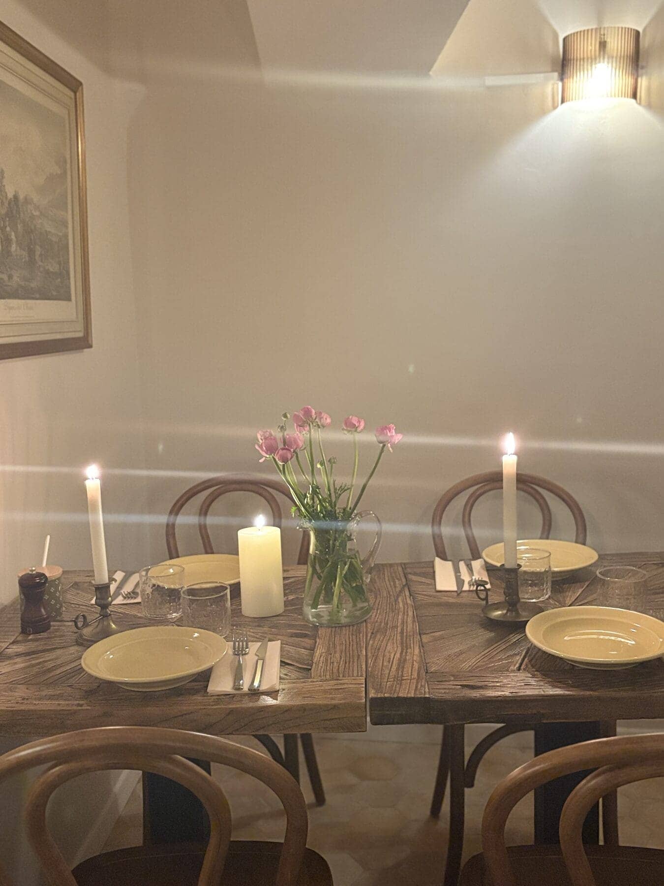 Table du Bistrot Napoléon dressée pour le service du soir : bougies allumées, fleurs roses et assiettes beiges.