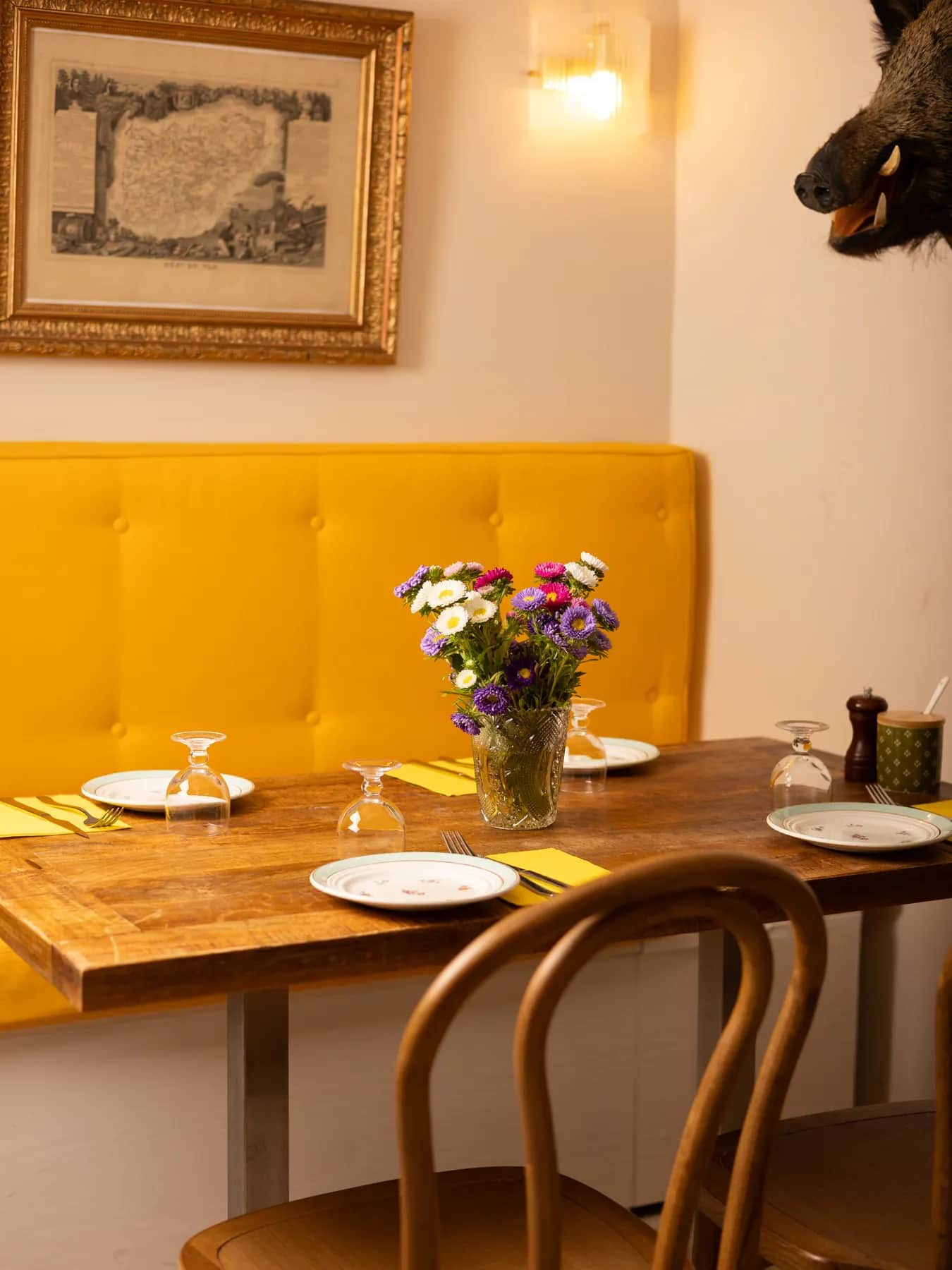 Table du soir dressée au Bistrot Napoléon, verres à pied, bouquet de fleurs fraîches et assiettes anciennes, prête pour un accord mets et vins corses.