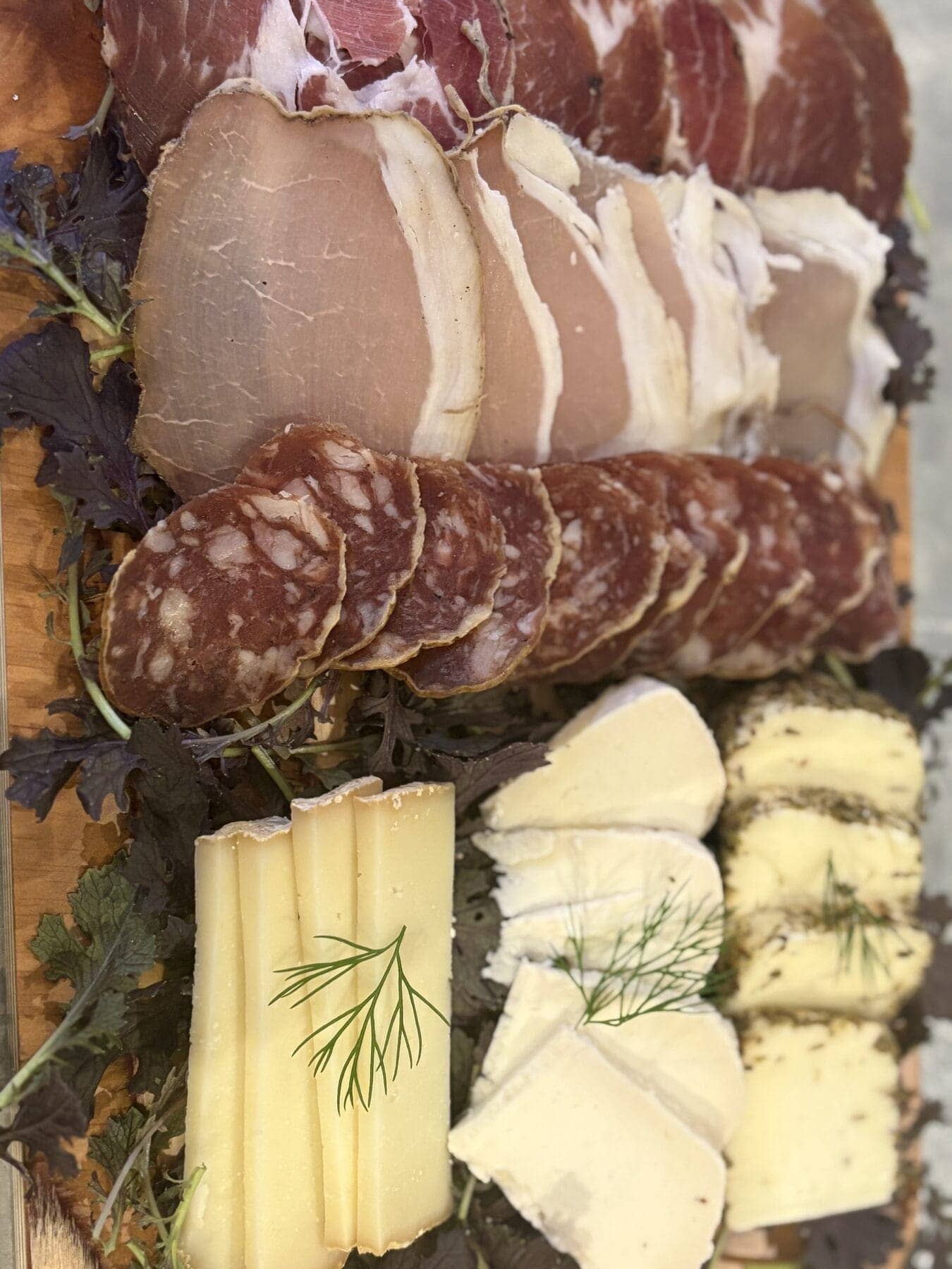 Planche de charcuteries corses et de fromages de brebis dressée sur une planche en bois, garnie d’herbes fraîches.