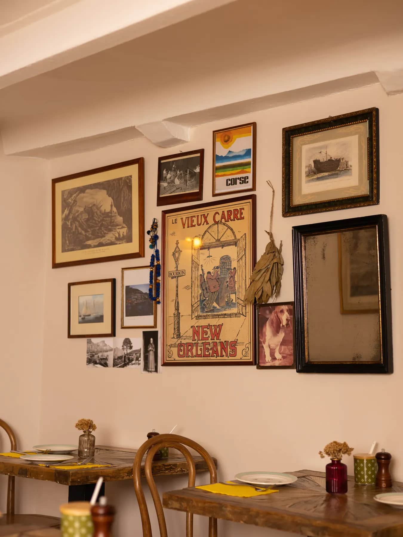 Coin de salle intimiste du Bistrot Napoléon à Hyères : tables en bois brut, chaises bistrot et mur d’objets chinés, prêt à réunir une famille pour un baptême.